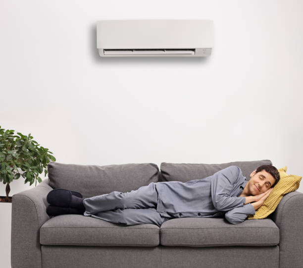 istock Man in pajamas sleeping on a sofa under an air conditioning unit 1289908751