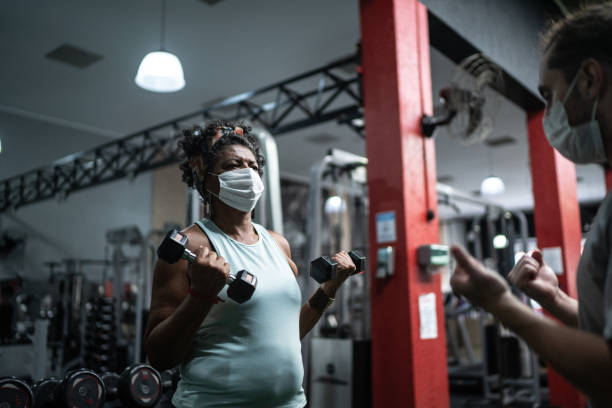 istock Senior woman training in the gym with instructor's assistance - using face mask 1289909151