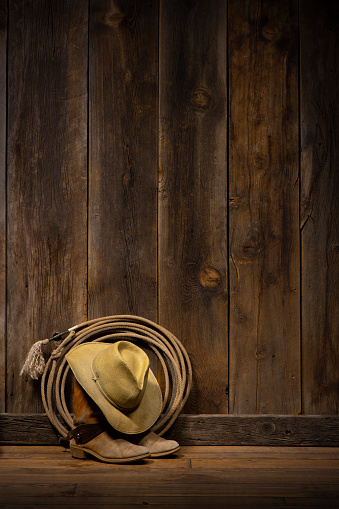 Wild West theme with a barn wood wall and floor with cowboy boots with spurs, hat and lasso. Most of the image is barn wood wall with large area for copy space.