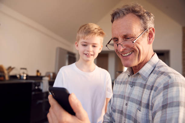 istock Grandson Showing Grandfather How To Solve Problem And Use Mobile Phone At Home 1289912948