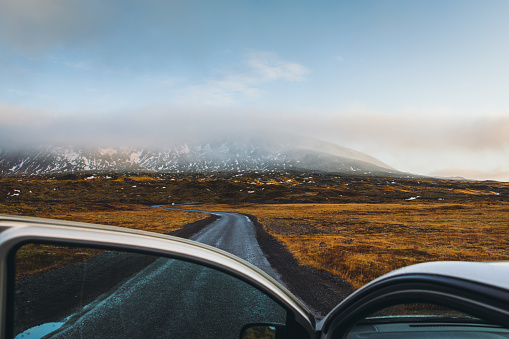 Scenic view of the picturesque asphalt road, golden meadow and snowcapped mountains during sunset - view from the car, road trip in Iceland