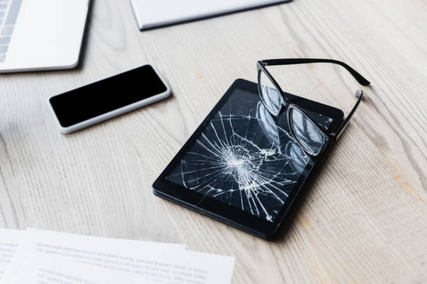 istock Eyeglasses on smashed digital tablet near documents and digital devices on wooden background 1289915809