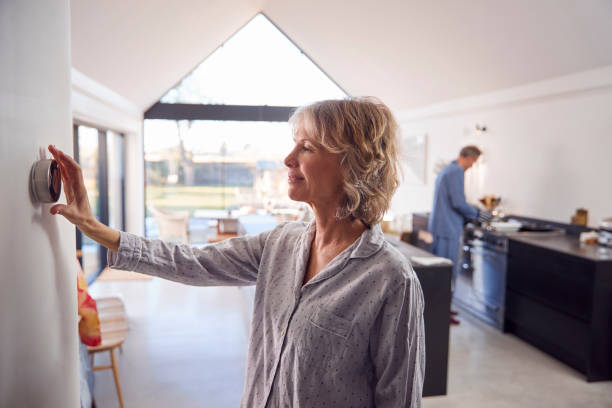 Mature Woman Adjusting Wall Mounted Digital Central Heating Thermostat Control At Home Mature Woman Adjusting Wall Mounted Digital Central Heating Thermostat Control At Home smart thermostat photos stock pictures, royalty-free photos & images