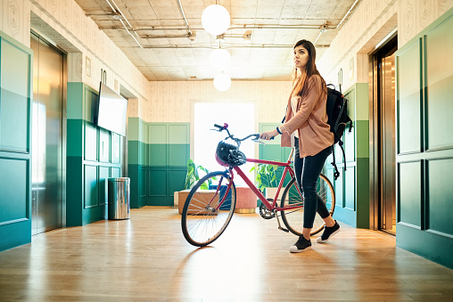 Young woman with backpack arriving at work by bicycle