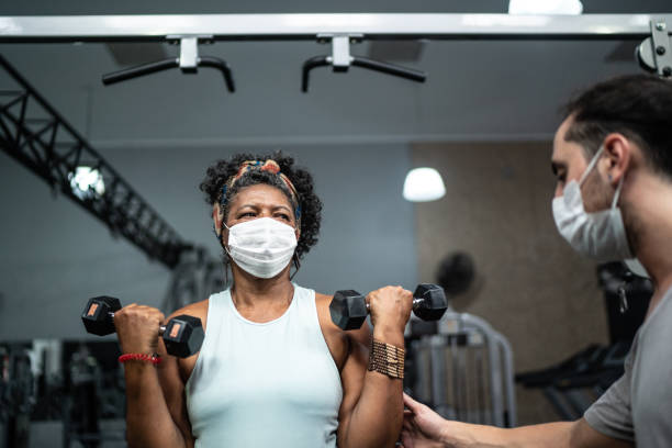 istock Senior woman training in the gym with instructor's assistance - using face mask 1289934785