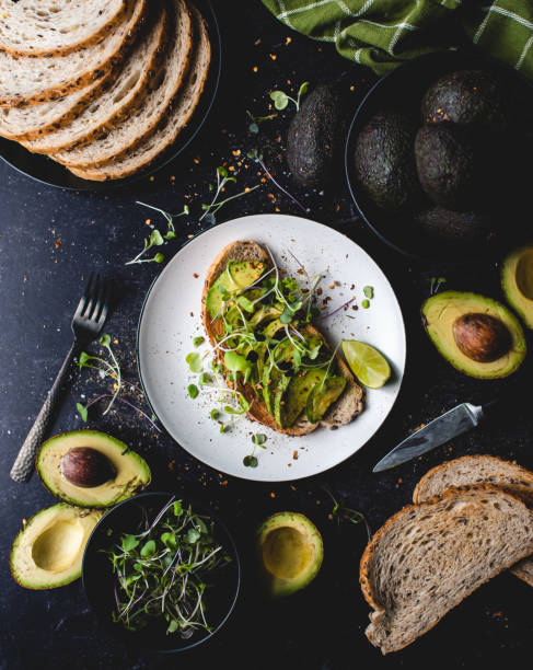 Avocado toast on a plate with ingredients around it on black counter.