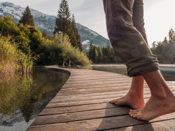 istock Low angle view of man walking barefoot across dock at sunrise 1289939003