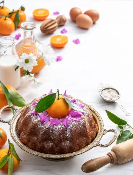 Bundt cake made of tangerine clementines baked homemade with ingredients on white wooden background