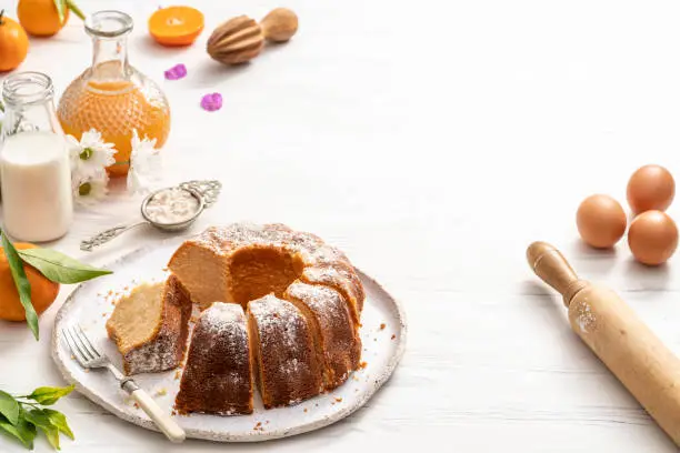 Bundt cake made of tangerine clementines baked homemade with ingredients on white wooden background