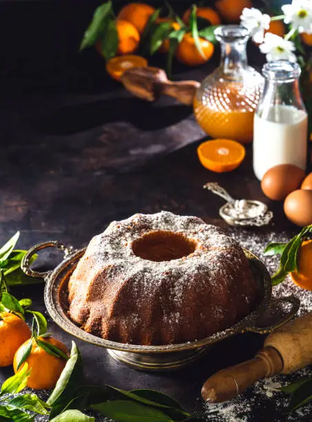 Bundt cake made of tangerine clementines baked homemade with ingredients on moody dark background