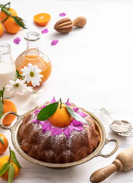 Bundt cake made of tangerine clementines baked homemade with ingredients on white wooden background