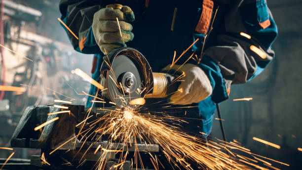 istock Locksmith in special clothes and goggles works in production. Metal processing with angle grinder. Sparks in metalworking 1289940767