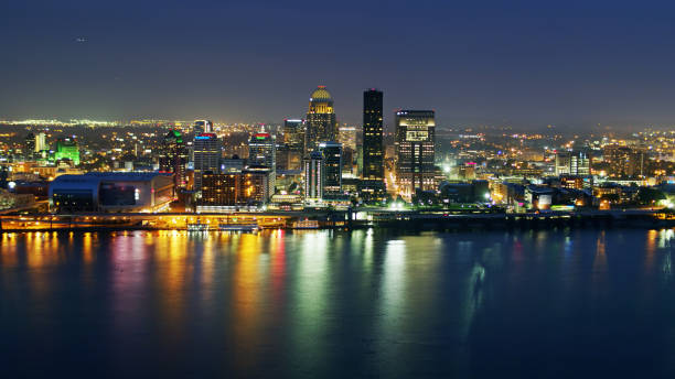 Louisville at Night Reflecting in Ohio River Aerial establishing shot of downtown Louisville, Kentucky on a summer evening, looking across the Ohio River towards the illuminated skyscrapers. louisville kentucky stock pictures, royalty-free photos & images