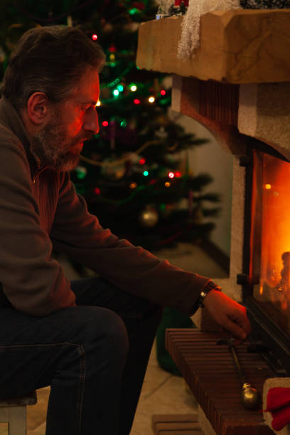istock Man sits in front of burning fireplace. Behind Christmas tree 1289942633