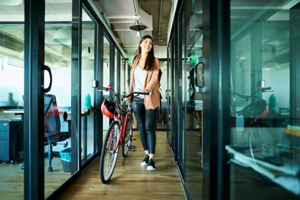 Businesswoman arriving to work on bike Young businesswoman pushing her bicycle and passing cubicles in the office office leave stock pictures, royalty-free photos & images