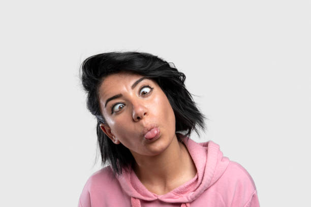 młoda zabawna kobieta robiąca głupie twarze na szarym tle - cross eyed making a face beautiful human face zdjęcia i obrazy z banku zdjęć