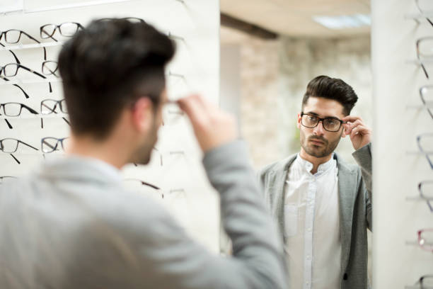 istock Man looking some glasses in optical store, trying on lenses and looking in mirror. Suit style. 1289945080