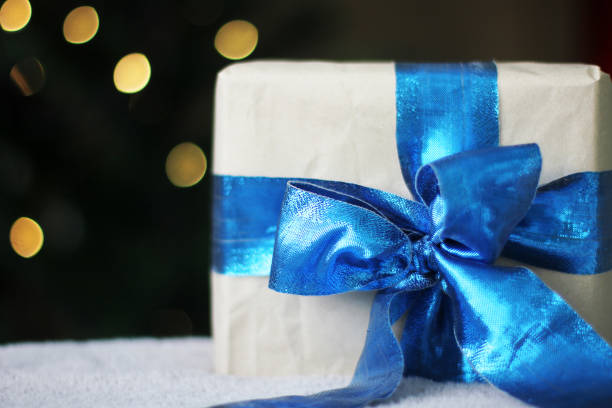 istock Gift with a blue bow and beautiful bokeh. Kraft paper packaging. Beautiful blue bow. A Christmas gift. New Year. Gift close-up. Orange blur 1289947780