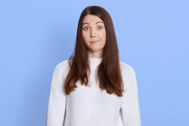 istock Young lovely female has dark hair, having misunderstanding expression, purses lips as being questionned, looks with puzzlement directly at camera, isolated over blue background. 1289951062