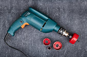 Saw crown and hand electric drill on gray background,  top view. Shallow depth of sharpness