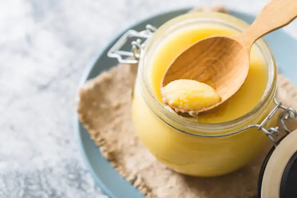 Photo of Ghee or clarified butter in jar and wooden spoon on gray table. Top view. Copyspace. Ghee butter have healthy fat and is a common cooking ingredient in many of the Indian food