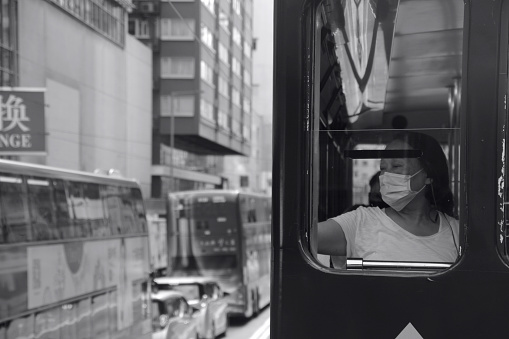 Woman wearing protective mask staring at the street from a double-decker tram in Hong Kong, during the coronavirus pandemic.