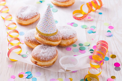 Stock photo showing close-up, elevated view of individual chocolate glazed ring doughnut decorated with white, pink, green, blue, yellow, and orange, hundred and thousand sugar sprinkles on blue background.