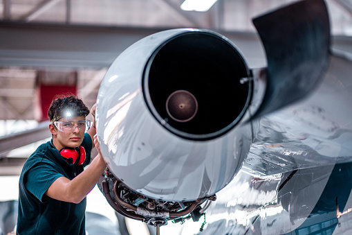 Airplane mechanic inspecting and checking the technology of a jet engine in the hangar at the airport.