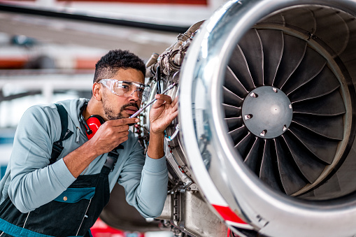 Young aircraft engineer in the hangar inspecting an airplane jet engine due to regular maintenance.