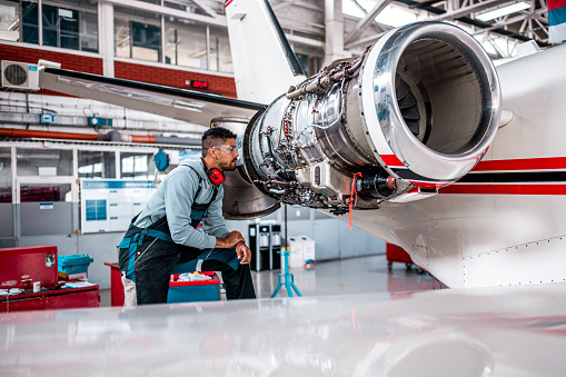 Young aircraft engineer in the hangar inspecting an airplane jet engine before the flight.