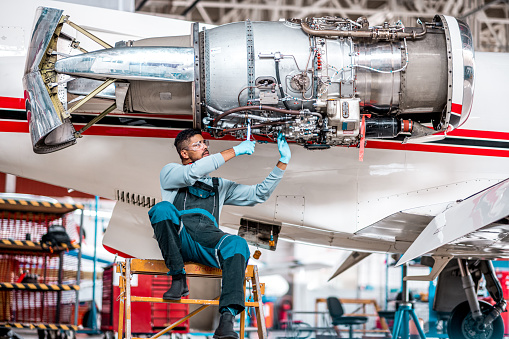 Aircraft engineer in the hangar repairing and maintaining an airplane jet engine.