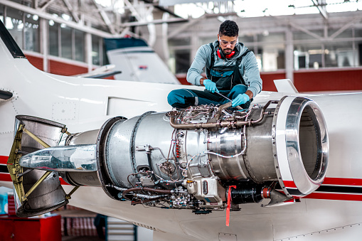 Young aircraft mechanic repairs an aircraft engine in the airport hangar.