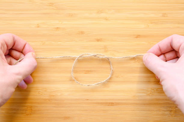 istock Human hands tie a knot on a rope on a wooden background. 1289964355
