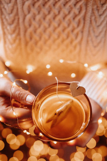 Young female hands holding a tea glass with a heart tea bag and christmas lights