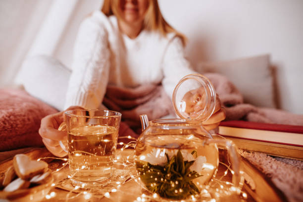 istock Young woman in cozy woolen pullover with winter blankets enjoying her blooming flower tea and light chain on the sofa 1289964455