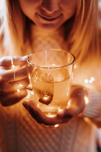 Young woman holding a tea glass with a tea bag with a heart shape and christmas lights