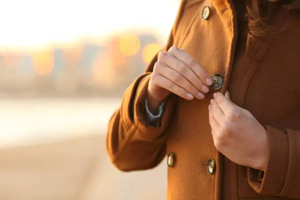 Lady fastening button of coat on the beach in winter