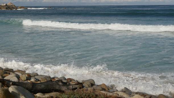 ondas oceânicas e rochas, monterey, norte da califórnia, eua. 17 milhas de carro perto de big sur, resort turístico de golfe à beira-mar na pacific coast highway. espirrando água e brisa do mar da praia de pebble. viagem - route 1 pacific ocean beach cliff - fotografias e filmes do acervo