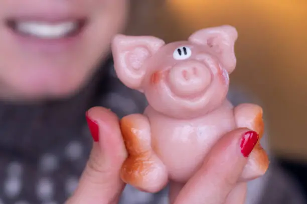 Woman with red nails holding a marzipan pink piglet dessert for new year, symbol of good furtune and prosperity