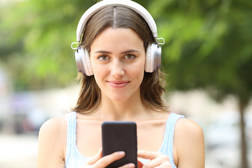 Woman wearing headphones holding phone looking at you
