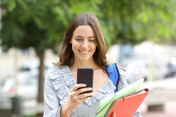 istock Happy student walks checking smart phone in the street 1289968503