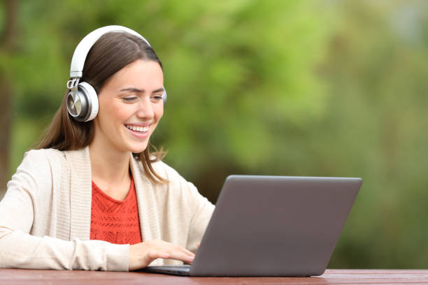 istock Happy woman using laptop and headphones in a park 1289968521