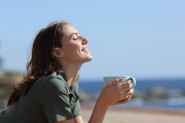 femme heureux retenant des respirations de tasse de café sur la plage - at the beach photos et images de collection