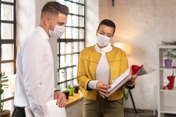 istock Colleagues standing at distance wearing protective face masks and discussing work at office during COVID-19 pandemic 1289971345