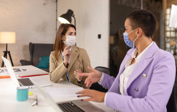 istock Businesswomen with face masks talking in office 1289972097