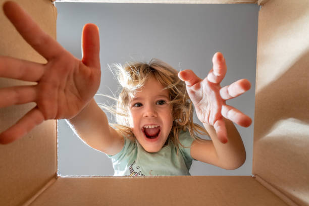 istock Happy little girl is opening gift and looking inside cardboard box. 1289973271