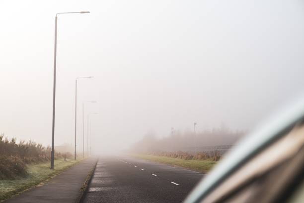 vue du côté passager d’une voiture d’une route et ses marques s’étendant dans la distance - asphalt two lane highway natural phenomenon fog photos et images de collection