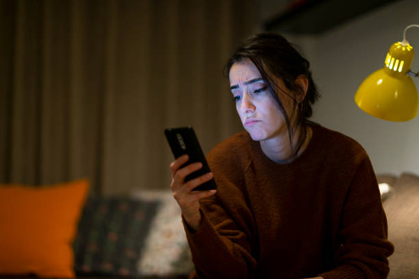 istock Woman looking at mobile phone screen feels upset at home at night time. 1289977208