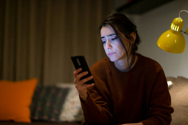istock Woman looking at mobile phone screen feels upset at home at night time. 1289977943