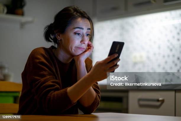 Woman Looking At Mobile Phone Screen Feels Upset At Home At Night Time Stock Photo - Download Image Now